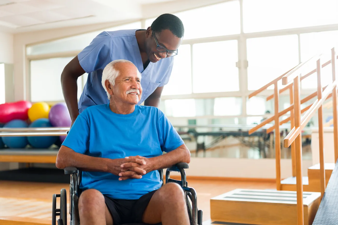 A healthcare professional assists an elderly man in a wheelchair during a physical therapy session in a rehabilitation center, promoting mobility and wellness.